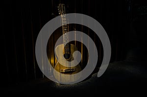 An wooden acoustic guitar is against a grunge textured wall. The room is dark with a spotlight for your copyspace