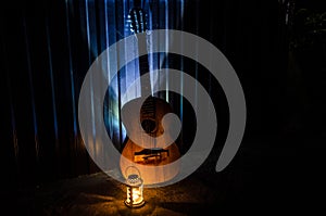 An wooden acoustic guitar is against a grunge textured wall. The room is dark with a spotlight for your copyspace