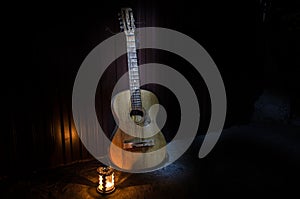 An wooden acoustic guitar is against a grunge textured wall. The room is dark with a spotlight for your copyspace