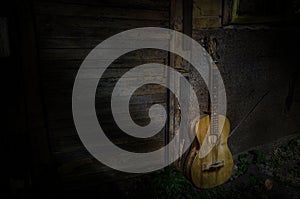 An wooden acoustic guitar is against a grunge textured wall. The room is dark with a spotlight for your copyspace