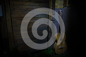 An wooden acoustic guitar is against a grunge textured wall. The room is dark with a spotlight for your copyspace