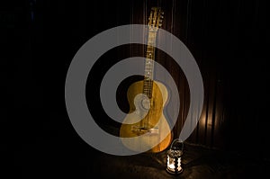 An wooden acoustic guitar is against a grunge textured wall. The room is dark with a spotlight for your copyspace