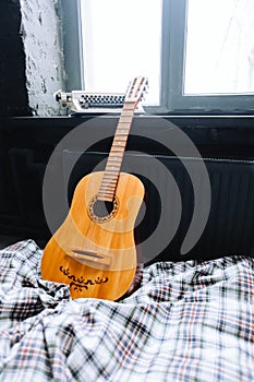 Wooden acoustic guitar on the bed near window