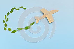 Wooden airplane model emitting fresh green leaves on blue background. Sustainable travel; clean and green energy; and biofuel