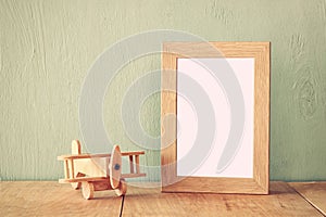 Wooden airplane toy over wood table next to blank photo frame. retro filtered image