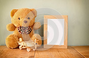 Wooden airplane toy and teddy bear over wood table next to blank photo frame. retro filtered image. ready to place photography