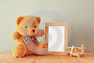 Wooden airplane toy and teddy bear over wood table next to blank photo frame. retro filtered image. ready to place photography