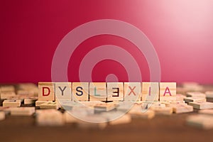 Wooden alphabet blocks with DYSLEXIA word in the center on wooden table against pink background