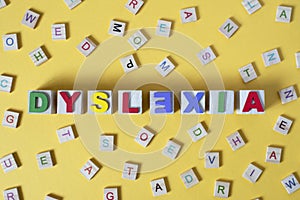 Wooden alphabet blocks with DYSLEXIA word in the center on yellow background