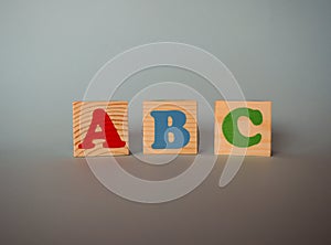 Wooden alphabet toy blocks with the text: abc. Isolated kids multi-colored ABC cubes on blue background