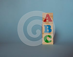 Wooden alphabet toy blocks with the text: abc. Isolated kids multi-colored ABC cubes on blue background with copy space.