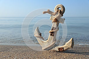 Wooden anchor with rope on sand near sea. Space for text