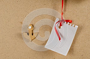 Wooden anchor. A sheet of paper hanging from a thin red ribbon v