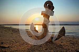 Wooden anchor on shore near river at sunset