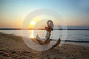 Wooden anchor on shore near river at sunset