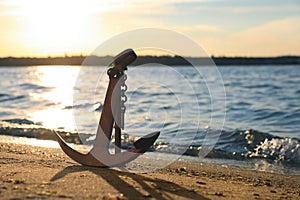 Wooden anchor on shore near river at sunset
