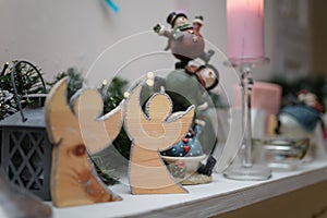 Wooden angel shaped toys standing on the fireplace on blurry toys background. Merry Christmas and winter holidays