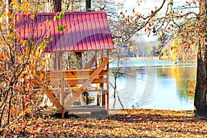 Wooden arbor with a table and picnic benches in the open air on the background of fallen leaves near a forest lake