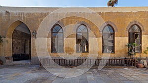 Wooden arched window with wrought iron grid over yellow stone bricks wall and arched passage