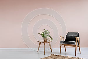 Wooden armchair with gray upholstery and a side table in a pastel pink living room interior with place for a bookcase. Real photo.