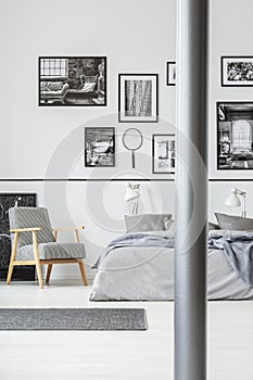 Wooden armchair next to bed in grey and white bedroom interior with gallery of photos. Real photo