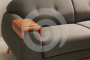 Wooden armrest table on sofa in room. Interior element