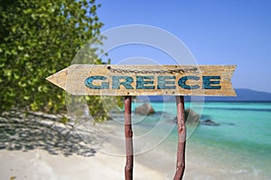 Wooden arrow road sign with word Greece against beach background. Travel to Greece concept