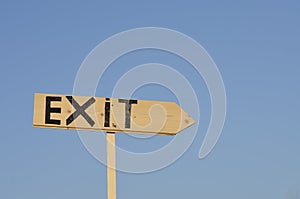 wooden arrow sign with the word exit. In the background the blue sky.