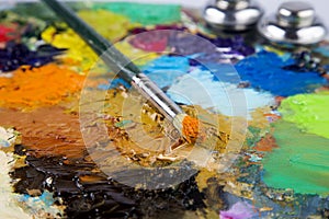 Wooden art palette with blobs of paint and a brush on white background