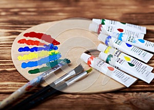 Wooden art palette with tubes of oil paints and a brush. Art and craft tools. Artist`s brush, canvas, palette knife. Space for tex