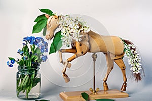Wooden articulated dummy horse mannequin in white inflorescences with a small bouquet of wild flowers