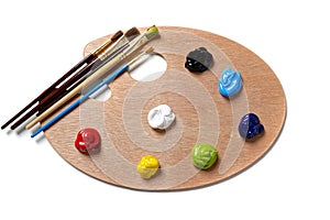 A wooden artists palette with bright colored paint and brushes