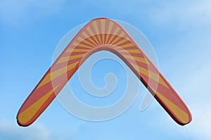 Wooden australian boomerang in flight against of pure white clouds and blue sky