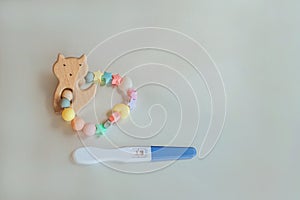 Wooden baby teether with beads and pregnancy test. Minimalistic flat lay with a wooden toys cat an isolated silver background. Toy