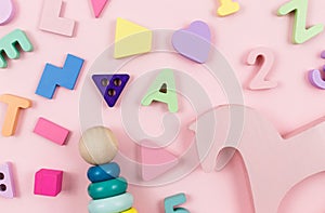 Wooden baby toys on a pastel pink background. Horse, numbers, blocks, puzzle shapes, pyramid,