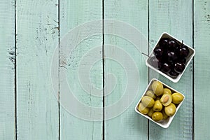 Wooden background with black olives, green olives, olive oil, fresh rosemary and spices. Flat lay.