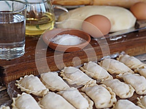 Wooden background with dumplings and dough ingredients for making dumplings. Food and cooking utensils on a brown kitchen board.