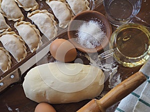 Wooden background with dumplings and dough ingredients for making dumplings. Food and cooking utensils on a brown kitchen board.