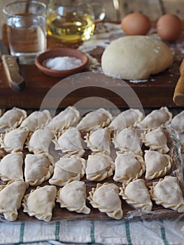 Wooden background with dumplings and dough ingredients for making dumplings. Food and cooking utensils on a brown kitchen board.