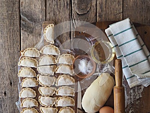 Wooden background with dumplings and dough ingredients for making dumplings. Food and cooking utensils on a brown kitchen board.