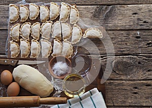 Wooden background with dumplings and dough ingredients for making dumplings. Food and cooking utensils on a brown kitchen board.