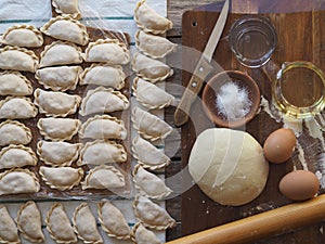 Wooden background with dumplings and dough ingredients for making dumplings. Food and cooking utensils on a brown kitchen board.