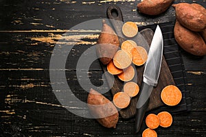 Cutting board and knife with raw sweet potato on wooden background