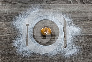 On a wooden background flour powder powdered snow silhouette plate plate fork knife appliances lies half orange mandarin orange