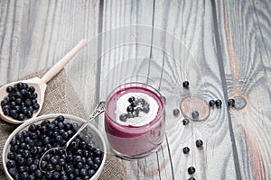 On a wooden background is a glass with a diet drink blueberry smoothie with whipped cream and a plate of blueberries on a napkin,