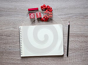 On a wooden background lies a blank sheet of a notebook on a spring pencil and a desk calendar cubes of red rowan September