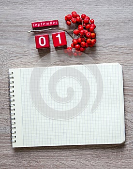 On a wooden background lies a blank sheet of a notebook on a spring pencil and a desk calendar cubes of red rowan September