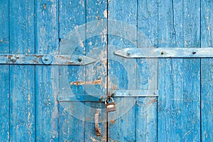 Wooden background. Old blue shabby wooden door with iron fasteners and a rusty lock. Torn up dilapidated boards. Natural creative