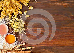 Wooden background spilled flour and egg with yolk near wheat stalks near spaghetti and pasta