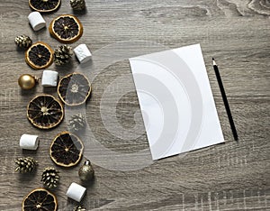 On a wooden background a white sheet and a black pencil and on the left a layout of dried oranges, balls, marshmallows